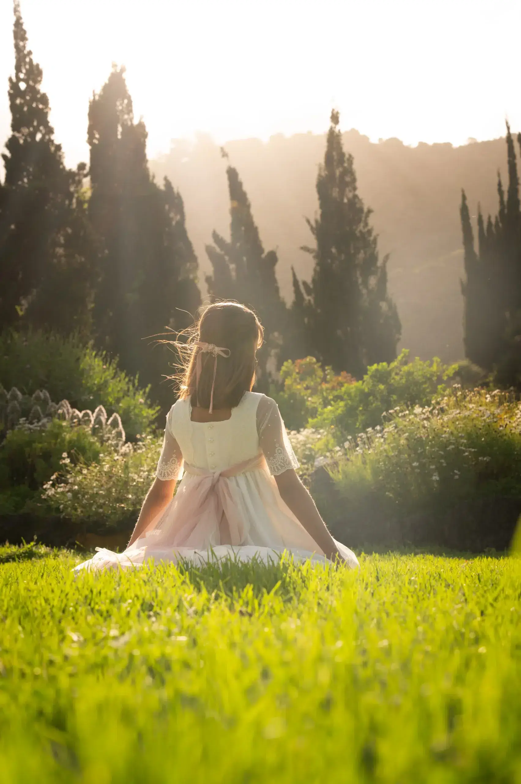 Niña con vestido de comunión en un jardín lleno de luz.