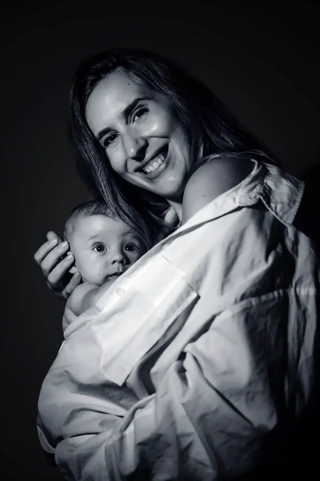 Una madre sonríe mientras sostiene a su bebé en un retrato en blanco y negro.