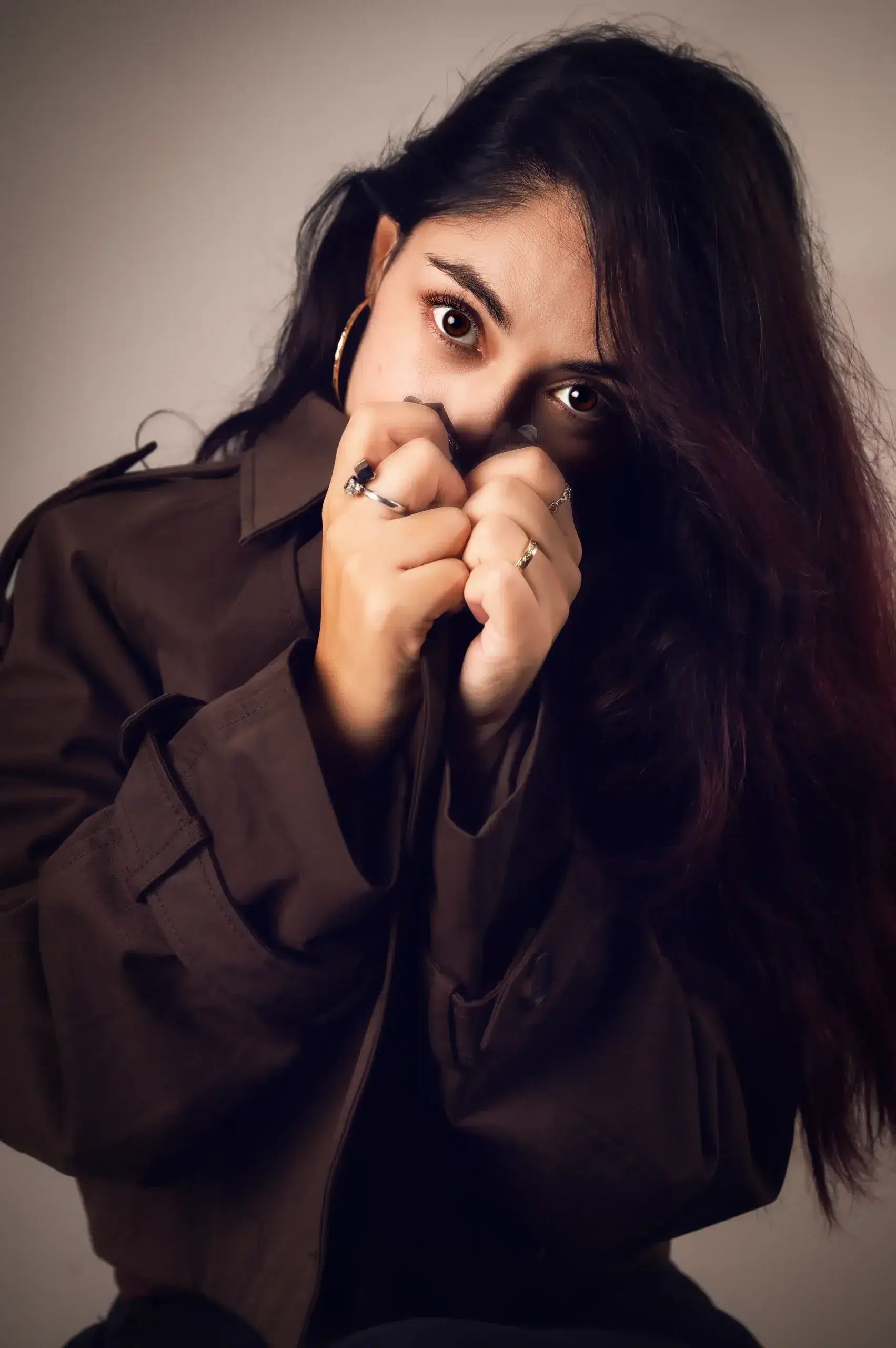 Retrato en estudio de una mujer de cabello oscuro con chaqueta marrón.